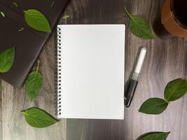 Still life photography blank notebook on wooden table with a cup of coffee, plant, leaf on table photo
