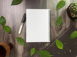 Still life photography blank notebook on wooden table with a cup of coffee, plant, leaf on table photo