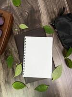 Still life photography blank notebook on wooden table with a cup of coffee, plant, leaf on table photo