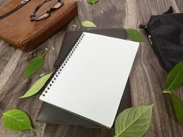 Still life photography blank notebook on wooden table with a cup of coffee, plant, leaf on table photo