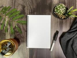 Still life photography blank notebook on wooden table with a cup of coffee, plant, leaf on table photo