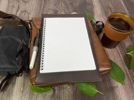 Still life photography blank notebook on wooden table with a cup of coffee, plant, leaf on table photo
