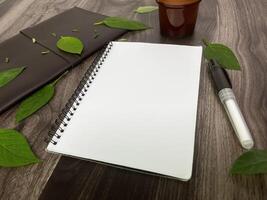 Still life photography blank notebook on wooden table with a cup of coffee, plant, leaf on table photo