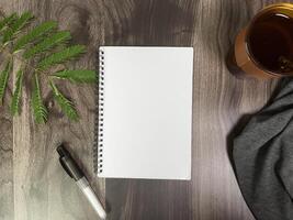 Still life photography blank notebook on wooden table with a cup of coffee, plant, leaf on table photo