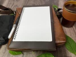 Still life photography blank notebook on wooden table with a cup of coffee, plant, leaf on table photo