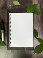 Still life photography blank notebook on wooden table with a cup of coffee, plant, leaf on table photo