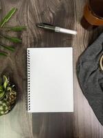 Still life photography blank notebook on wooden table with a cup of coffee, plant, leaf on table photo