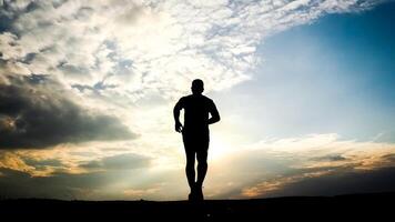 Silhouette of a Man Running at Sunset with Dramatic Sky and Clouds in the Background photo