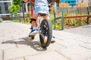 Close up view of legs of little girl rides a two-wheeled bicycle Ii the courtyard of apartment buildings in summer, Europe. High quality photo
