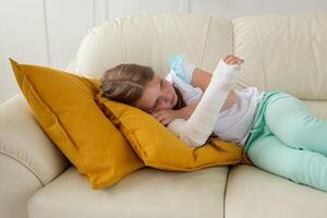 Child with a cast on a broken wrist or arm lying on a couch. Recovery and disease concept. photo