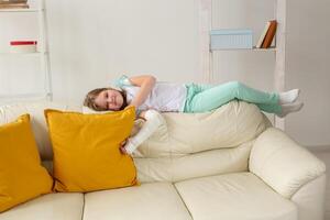 Child with a cast on a broken wrist or arm smiling and having fun on a couch. Positive attitude, recovery and kid concept. photo