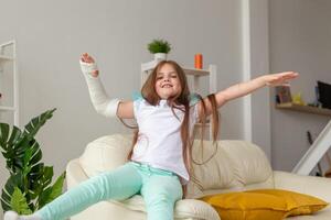 Child with a cast on a broken wrist or arm smiling and having fun on a couch. Positive attitude, recovery and kid concept. photo
