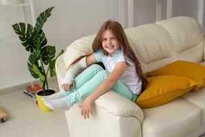 Child with a cast on a broken wrist or arm smiling and having fun on a couch. Positive attitude, recovery and kid concept. photo