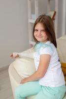 Child with a cast on a broken wrist or arm smiling and having fun on a couch. Positive attitude, recovery and kid concept. photo