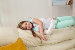 Child with a cast on a broken wrist or arm smiling and having fun on a couch. Positive attitude, recovery and kid concept. photo