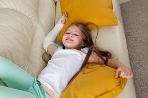 Child with a cast on a broken wrist or arm smiling and having fun on a couch. Positive attitude, recovery and kid concept. photo