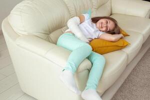 Child with a cast on a broken wrist or arm smiling and having fun on a couch. Positive attitude, recovery and kid concept. photo