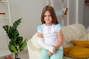Child with a cast on a broken wrist or arm smiling and having fun on a couch. Positive attitude, recovery and kid concept. photo