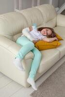 Child with a cast on a broken wrist or arm smiling and having fun on a couch. Positive attitude, recovery and kid concept. photo
