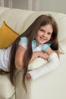 Child with a cast on a broken wrist or arm sits on a couch. Recovery and kid concept. photo
