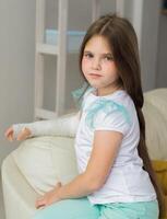 Child with a cast on a broken wrist or arm sits on a couch. Recovery and kid concept. photo