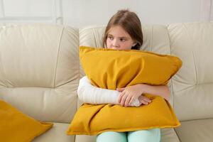 Child with a cast on a broken wrist or arm sitting on a couch. Recovery and disease concept. photo