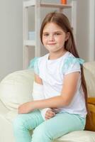 Child with a cast on a broken wrist or arm smiling and having fun on a couch. Positive attitude, recovery and kid concept. photo