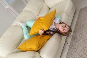 Child with a cast on a broken wrist or arm smiling and having fun on a couch. Positive attitude, recovery and kid concept. photo
