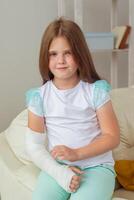 Child with a cast on a broken wrist or arm smiling and having fun on a couch. Positive attitude, recovery and kid concept. photo