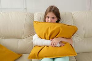 Child with a cast on a broken wrist or arm sitting on a couch. Recovery and disease concept. photo