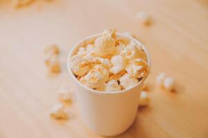 A bucket of popcorn, top-view, warm colors, light brown wooden background, flat lay, daylight macro close-up photo