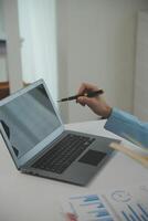Charming Young asian businesswoman sitting on laptop computer in the office, making report calculating balance Internal Revenue Service checking document. photo