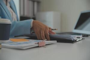 Charming Young asian businesswoman sitting on laptop computer in the office, making report calculating balance Internal Revenue Service checking document. photo
