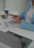 Charming Young asian businesswoman sitting on laptop computer in the office, making report calculating balance Internal Revenue Service checking document. photo