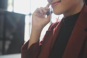 Friendly female helpline operator in call center. Young woman working in call center and holding microphone on headset with hand. photo