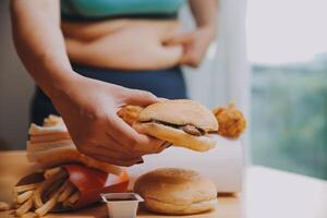 To eat or not. Cheerless plump woman looking at the burger while thinking to eat it or not photo