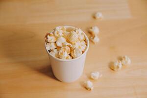 A bucket of popcorn, top-view, warm colors, light brown wooden background, flat lay, daylight macro close-up photo