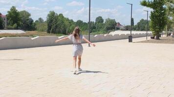 A beautiful, attractive and happy young woman is walking and running in the center of a city park in the summer season in the afternoon, slow motion video