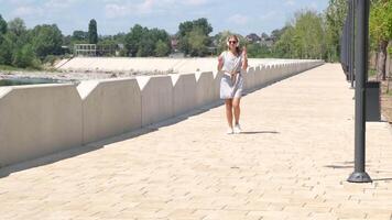 A beautiful, attractive and happy young woman is walking in the center of a city park in the summer season in the afternoon. listening to the music video