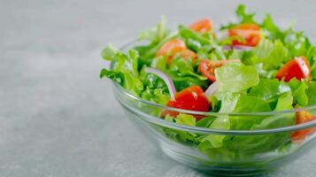 Fresh Green Salad in Glass Bowl with Cherry Tomatoes and Red Onion on Gray Background, Healthy Eating, Vegan Diet, Mediterranean Cuisine, Bright and Colorful Food, Close-Up View photo