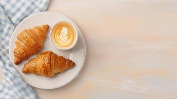 Overhead View of a Delicious Breakfast Scene Featuring Croissants and a Latte with Creamy Latte Art on a White Plate with a Blue Checkered Napkin on a Light Wood Background for a Cozy Morning Vibe photo