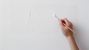 Close Up of a Person's Hand Holding a Paintbrush Poised Above a White Canvas with Textured Paint for Artistic Creation and Creative Process Concept in Minimalist Style photo