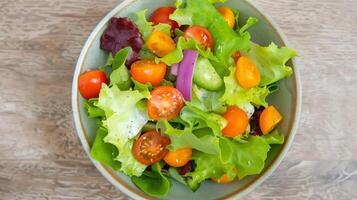 Overhead View of Fresh Colorful Garden Salad with Cherry Tomatoes, Cucumbers, Mixed Greens in Ceramic Bowl on Wooden Surface photo