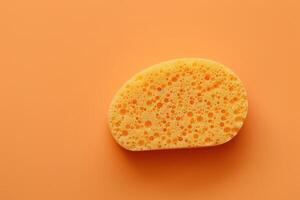Yellow kitchen sponge on a vibrant orange background photo