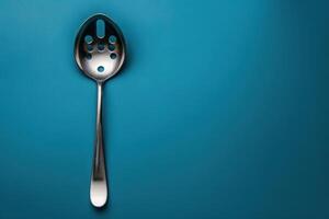 Metal slotted spoon resting on a blue background photo