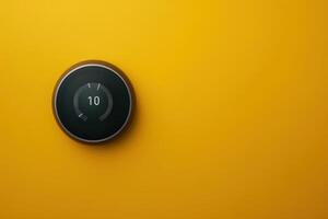 Modern smart thermostat on vibrant yellow wall displaying temperature settings photo