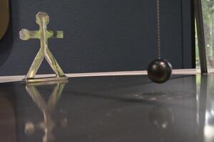 A metal human figure and a pendulum ball near it. The concept of human endurance and resilience in the face of adversity and difficulties. photo
