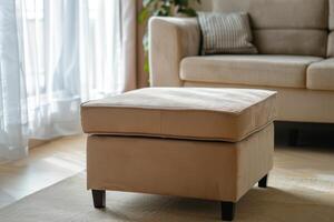 Cozy living room with a beige ottoman, plush sofa, and natural light through curtains photo