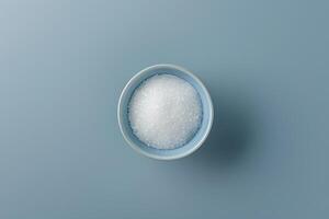 Bowl of granulated sugar on a blue surface photo