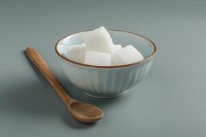 Sugar cubes in a bowl with a wooden spoon on a gray surface photo